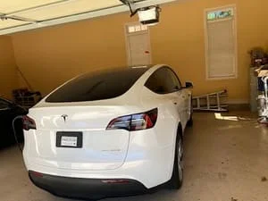 White electric SUV parked in garage beside a wall-mounted EV charger installation