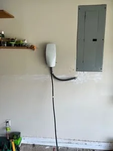 Wall-mounted EV charger with black conduit beside gray metal electrical panel on drywall