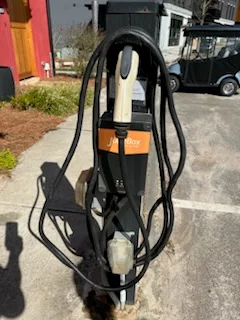 Black and orange EV charging station with coiled cables and white plug on a pedestal in a paved parking lot