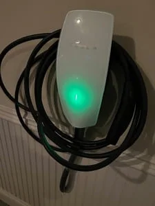White wall-mounted EV charger with green indicator light and coiled black charging cable