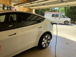 White electric SUV charging in a garage with a cable connected to a wall-mounted EV charger