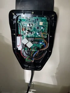 Open black EV charger housing with green circuit board, relays, and colored wiring exposed on a wall-mounted unit