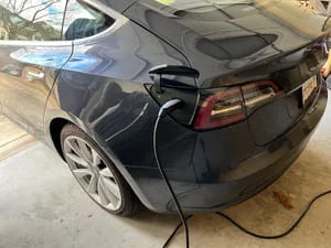 Dark blue electric vehicle connected to a wall-mounted EV charger with cable in a garage
