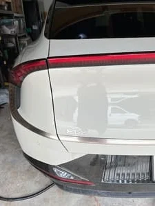 White electric vehicle rear with charging cable connected to charge port beside red taillight in a garage