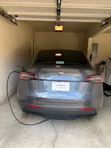 Gray electric vehicle charging in a garage with a black charging cable connected to a wall-mounted EV charger