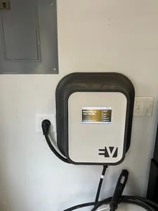 Wall-mounted EV charger with black charging cable beside an electrical panel and wall outlet