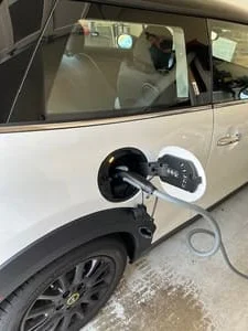 White electric vehicle with charging cable connected to the charge port on a concrete floor