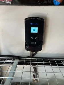 Wall-mounted EV charger with blue display screen mounted above a metal cable tray