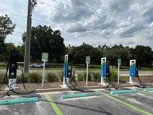 Four DC fast-charging stations on concrete pedestals with teal curb islands and striped parking stalls