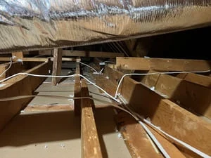 Attic with white cable runs routed across exposed wood ceiling joists and silver-wrapped ductwork above