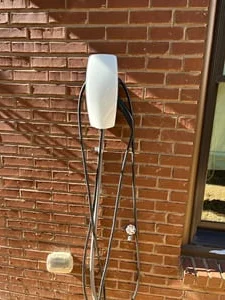 White wall-mounted EV charger with black coiled cables on a red brick exterior wall beside a window