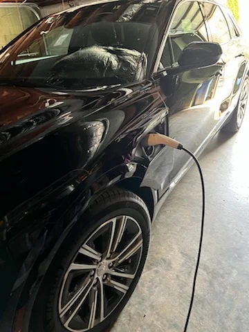 Black electric SUV connected to a charging cable in a garage with a concrete floor