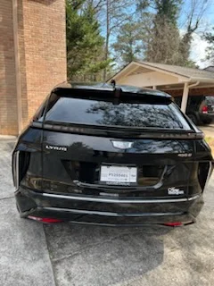 Black Cadillac electric SUV parked in a driveway beside a brick house with a carport
