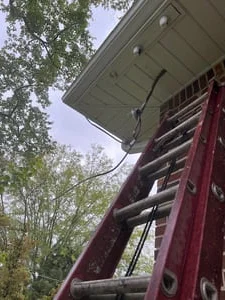Red extension ladder against brick wall with black cable run along white soffit and fascia at eave