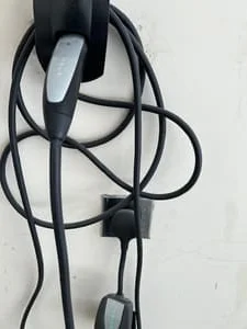 Black EV charging cables with gray connector coiled on wall-mounted holders against a white wall